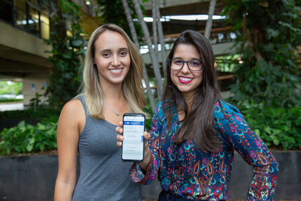 As servidoras da SAA Milena Gomes e Carolina Bardella mostram o acesso aos documentos digitais pelo celular. Foto: André Reis / Secom UnB.